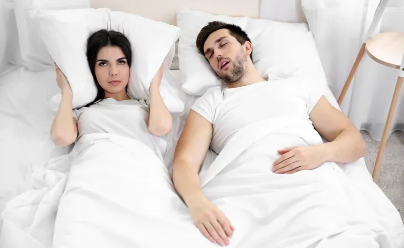 man-snoring-woman-covering-ears-with-pillow